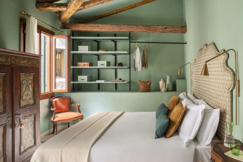 Sage green bedroom featuring a bed with pattern headboard, open shelving, and exposed rustic wood ceiling beams - Hotel Riva, BZAR hotels in Venice