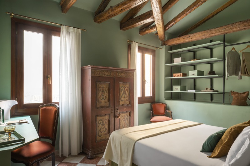 Green bedroom with beamed ceiling, antique painted wardrobe, green desk, and vintage orange chair - Hotel Riva, BZAR hotels in Venice