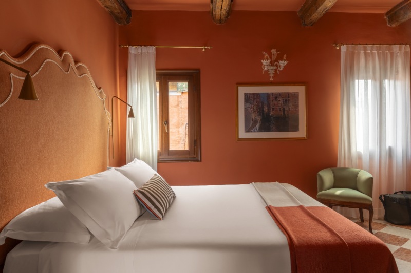Bed detail with striped pillow, brass reading lights, and distinctive upholstered headboard against terracotta walls - Hotel Riva, BZAR hotels in Venice
