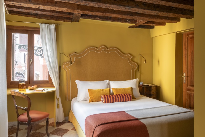 Triple room with mustard yellow walls, rustic wooden beams, and a writing desk by the window - Hotel Riva, BZAR hotels in Venice