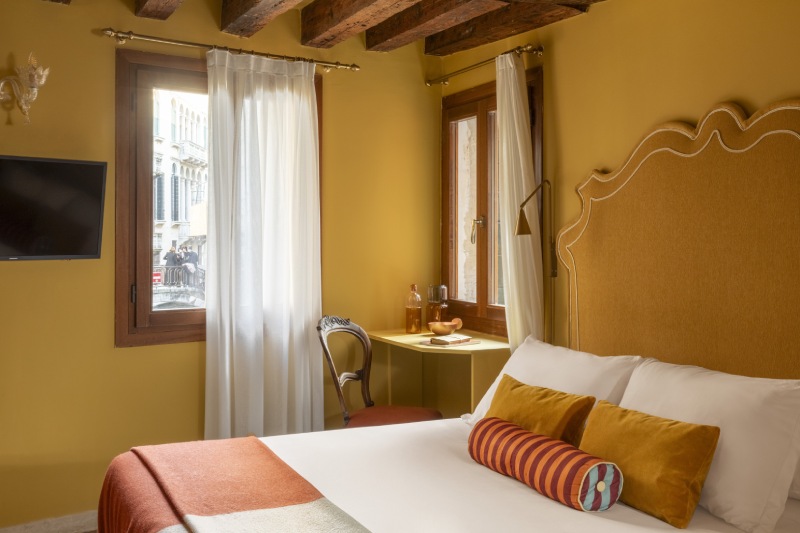 Bright triple room featuring mustard walls, decorative pillows, wall-mounted TV, and a glimpse of Venice - Hotel Riva, BZAR hotels in Venice